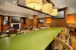 A restaurant with a long green table, wooden chairs, and a fireplace. - Fairfield Inn & Suites Germantown Gaithersburg (Germantown)