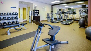 Un gimnasio con equipo de ejercicio, una banca, mancuernas, cintas de correr y un espejo grande.