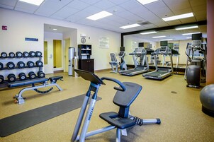 Un gimnasio con equipo de ejercicio, una banca, mancuernas, cintas de correr y un espejo grande.