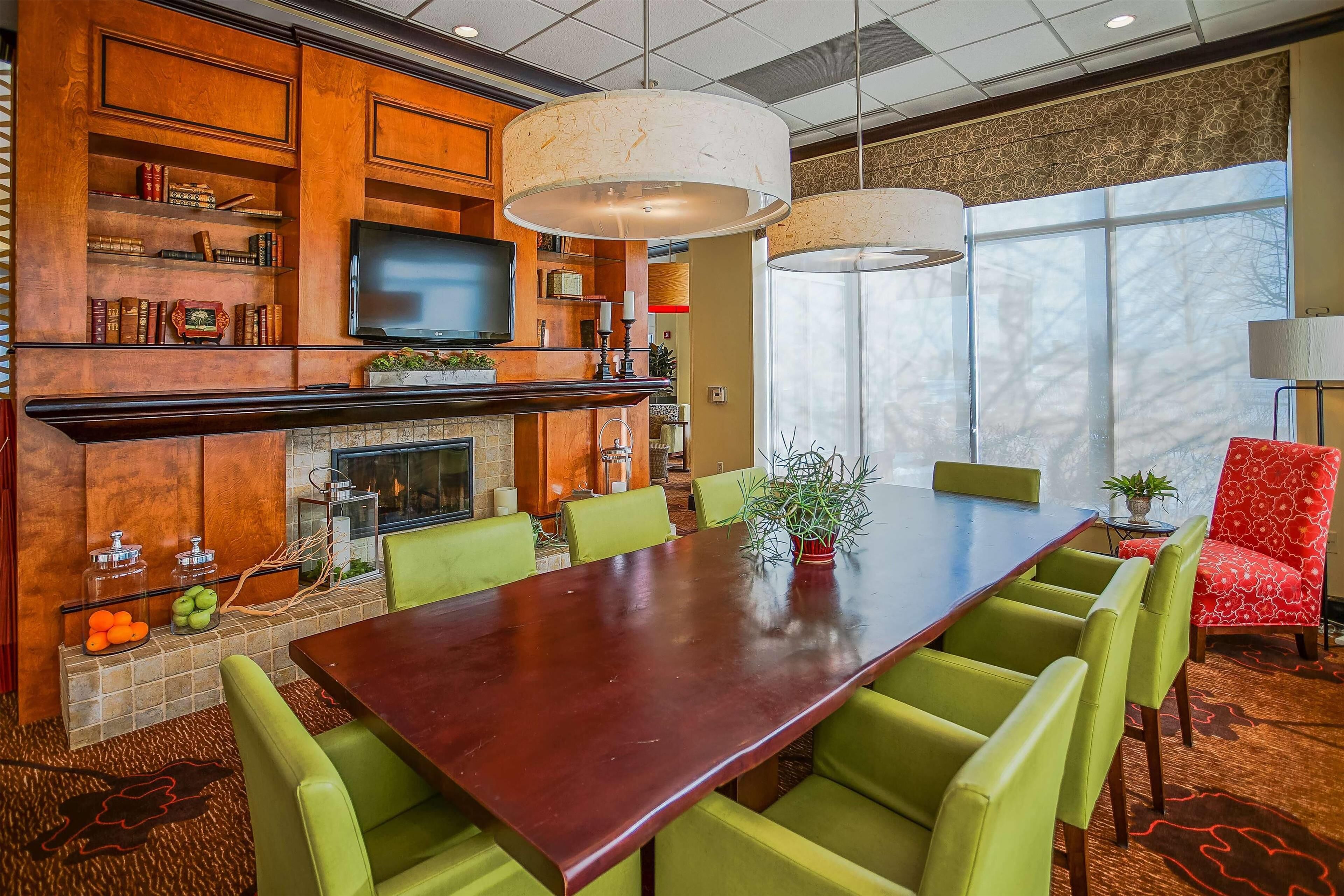 A conference room with a long wooden table, green chairs, a television, bookshelves, and a fireplace.