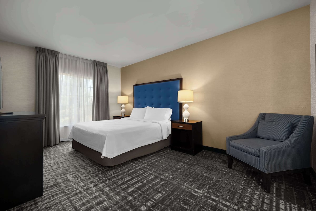 Una habitación de hotel con una cama grande, una silla, un escritorio y una lámpara.