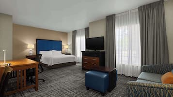 A hotel room with a bed, a desk, a TV, a sofa, and curtains.