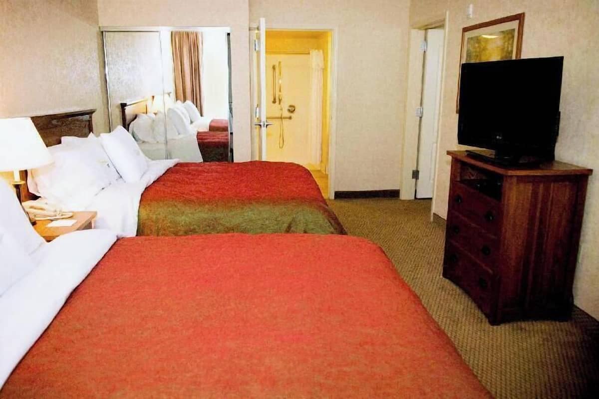 Habitación de hotel con dos camas, televisión, cómoda y puerta de baño.