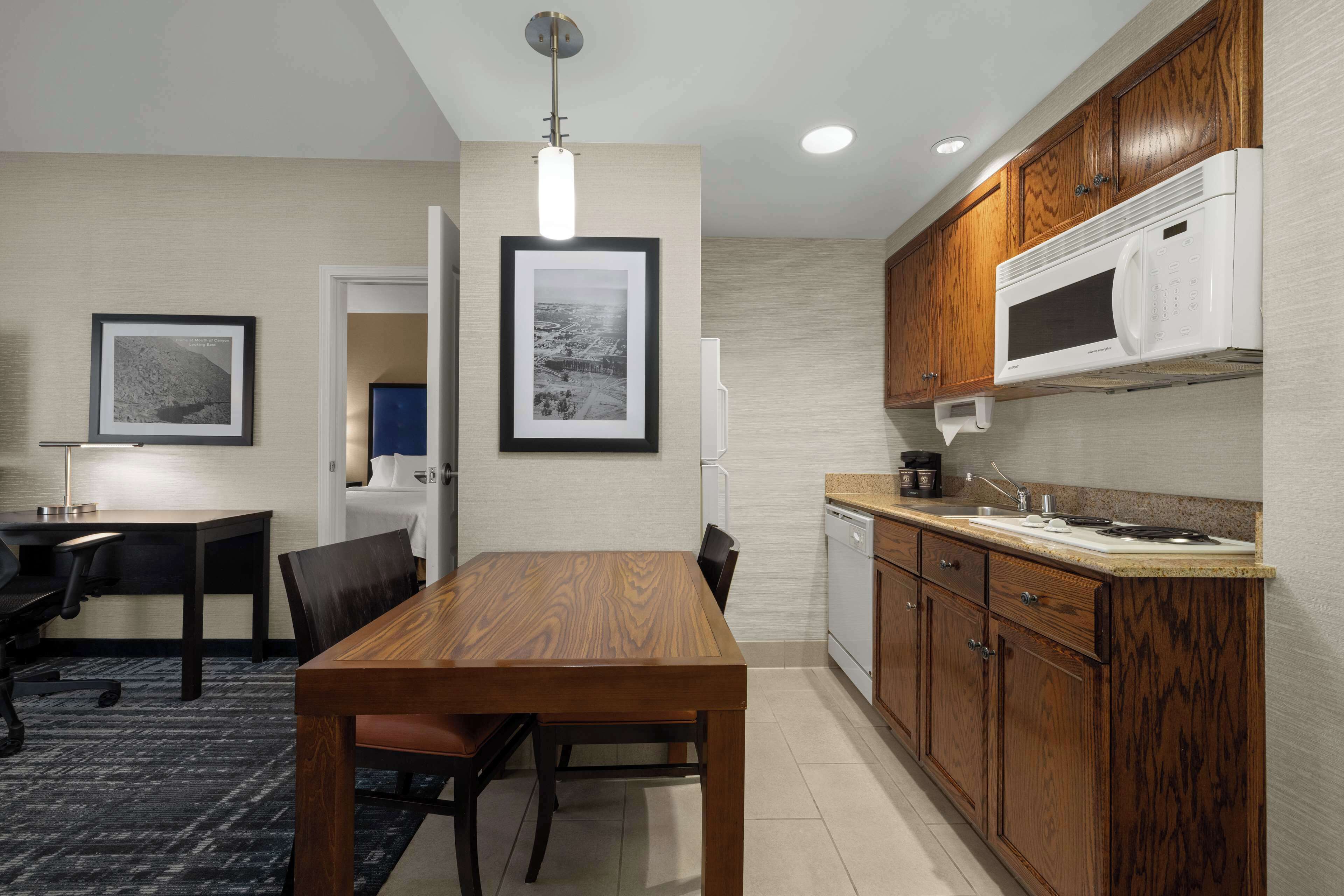 A modern kitchen with wooden cabinets, a built-in microwave, and a dining area with a table and chairs.