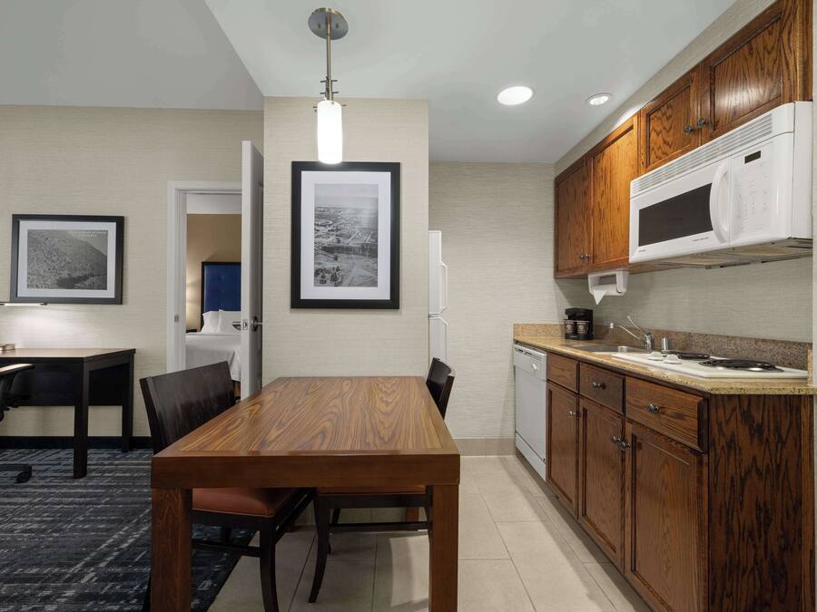 A modern kitchen with wooden cabinets, a built-in microwave, and a dining area with a table and chairs.