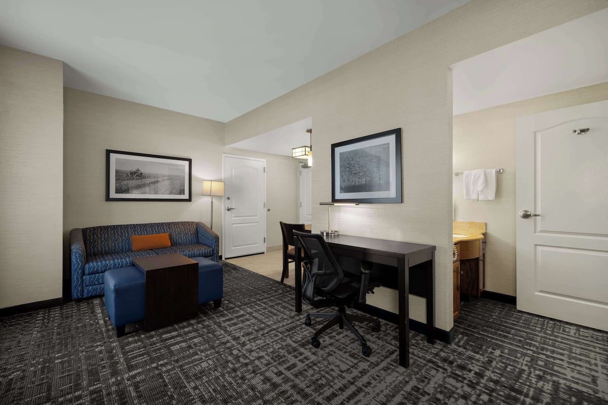 Habitación de hotel con sofá, escritorio, silla, lámpara y cuadros en la pared.