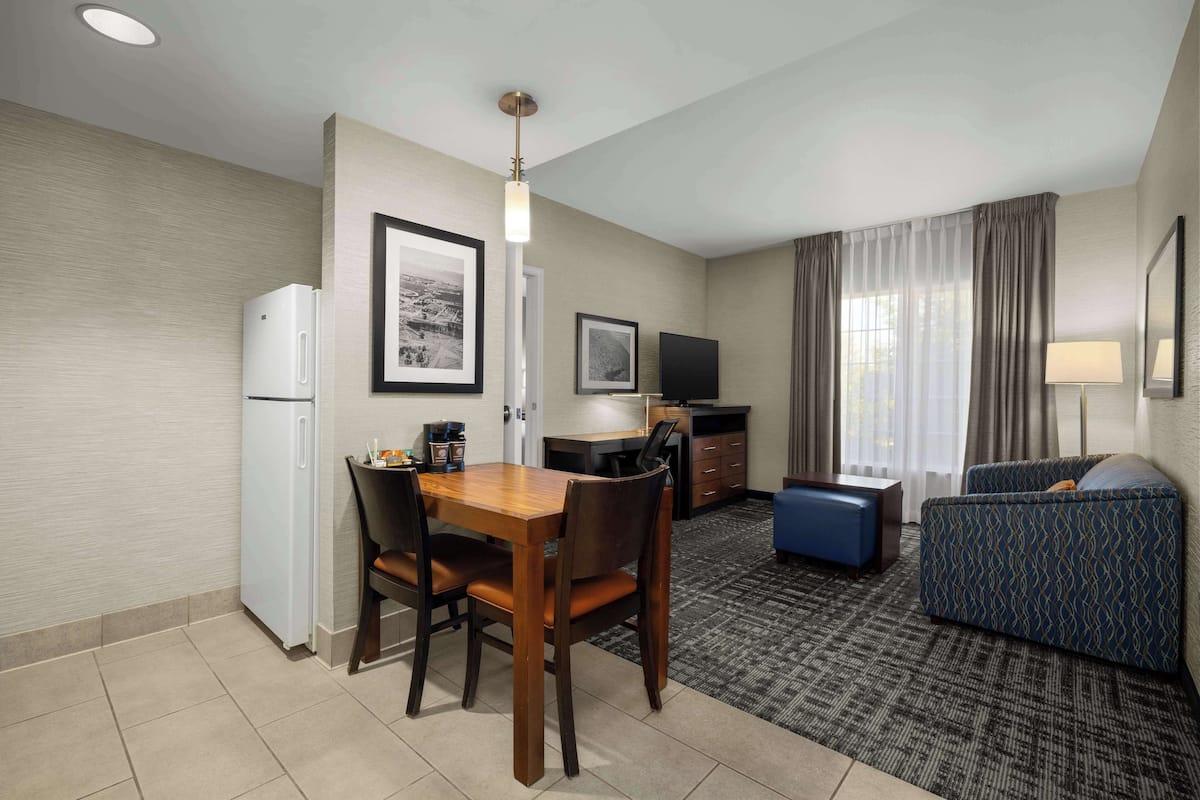 Habitación de hotel con una mesa de comedor, sillas, un sofá, televisor, refrigerador y lámpara.