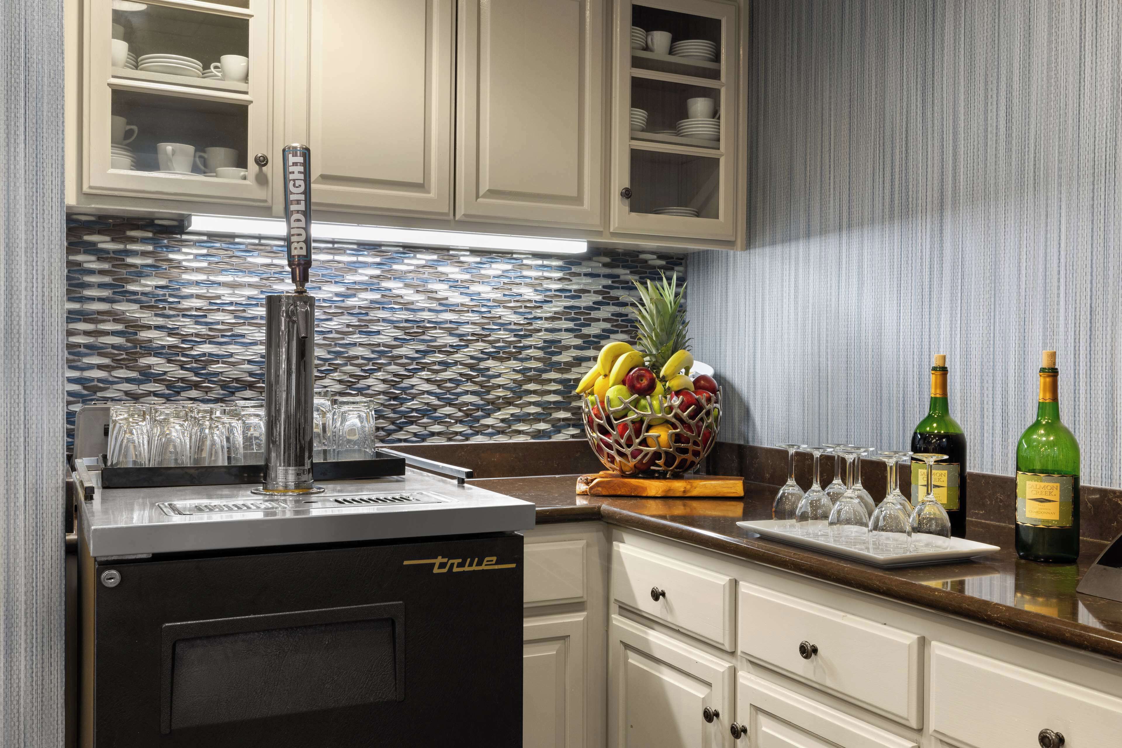 A kitchen with a beer tap, a fruit bowl, and wine bottles.