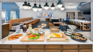 Eine moderne Cafeteria mit verschiedenen Sitzbereichen, einem Buffet mit vielfältigen Speisen und einem an der Wand befestigten Fernseher.