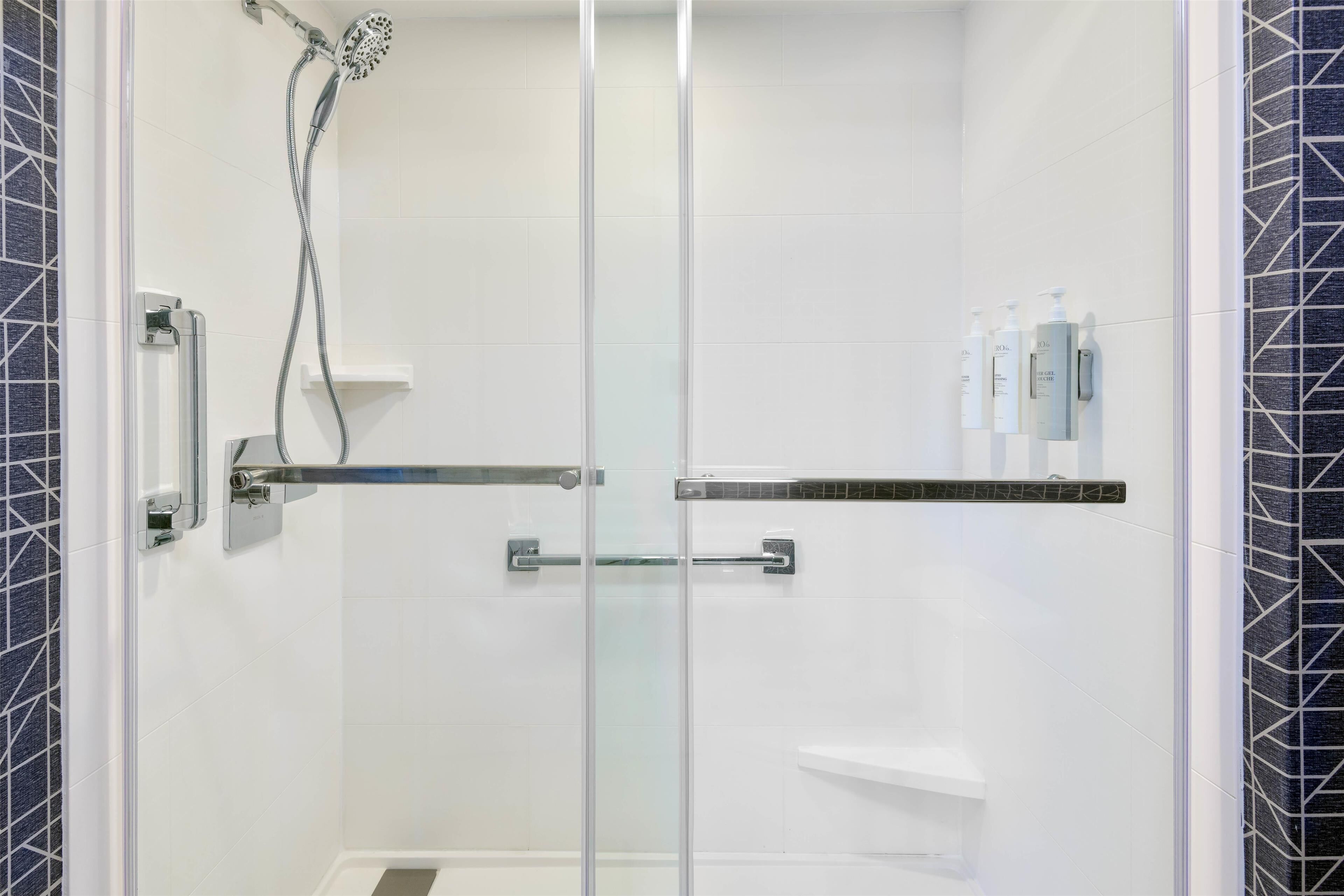 Ein modernes Duschbad mit Glastür, Handbrause und Ablage für Toilettenartikel.