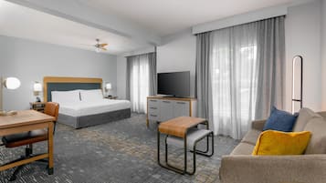 Habitación de hotel con cama, escritorio, silla, sofá, televisión y ventilador de techo.