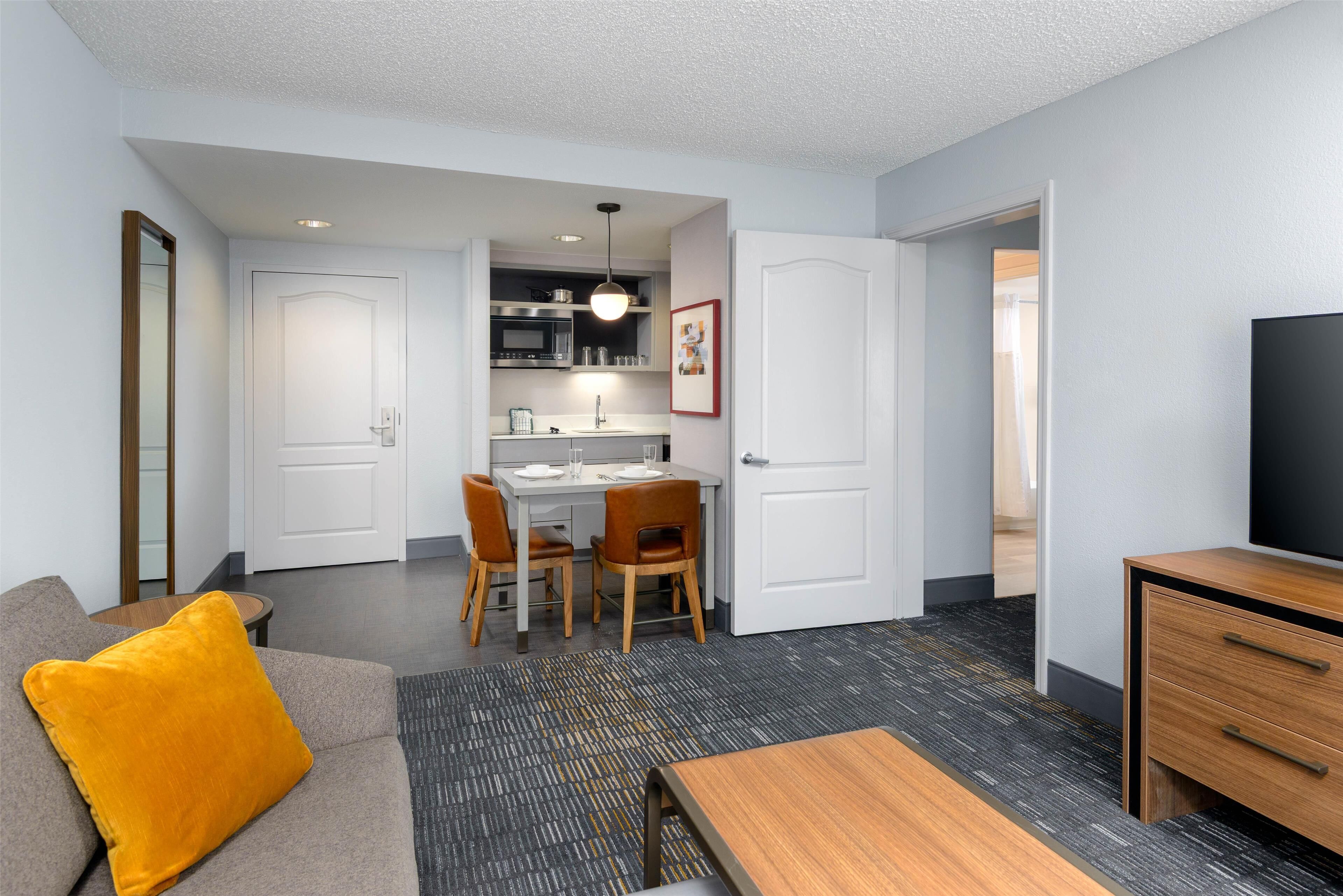 A compact living space with a sofa, a dining table with chairs, a kitchenette, and a TV.