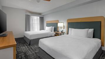 A hotel room with two beds, a desk, a ceiling fan, and a window with curtains.