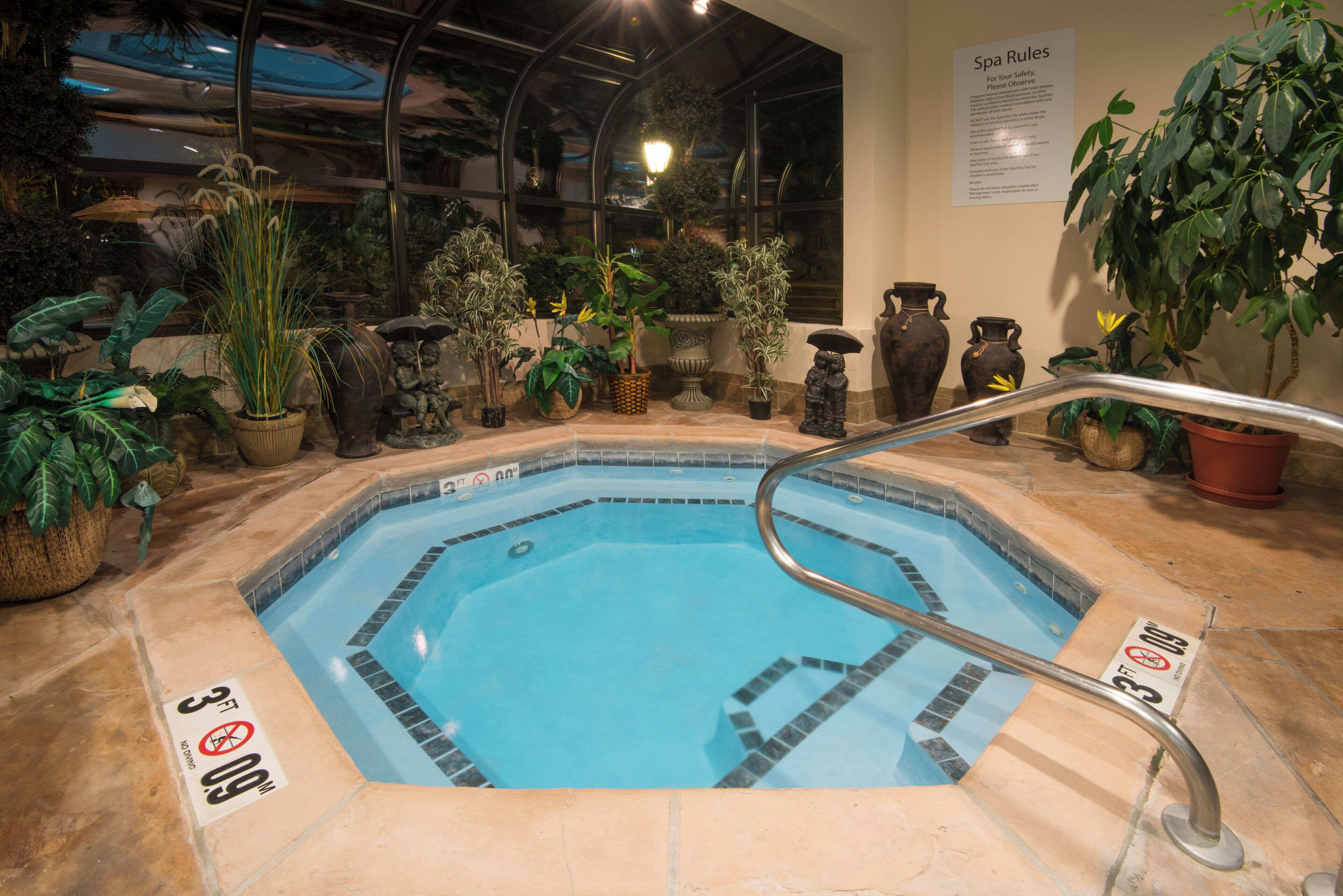 An indoor swimming pool with a glass enclosure, surrounded by potted plants and decorative items.