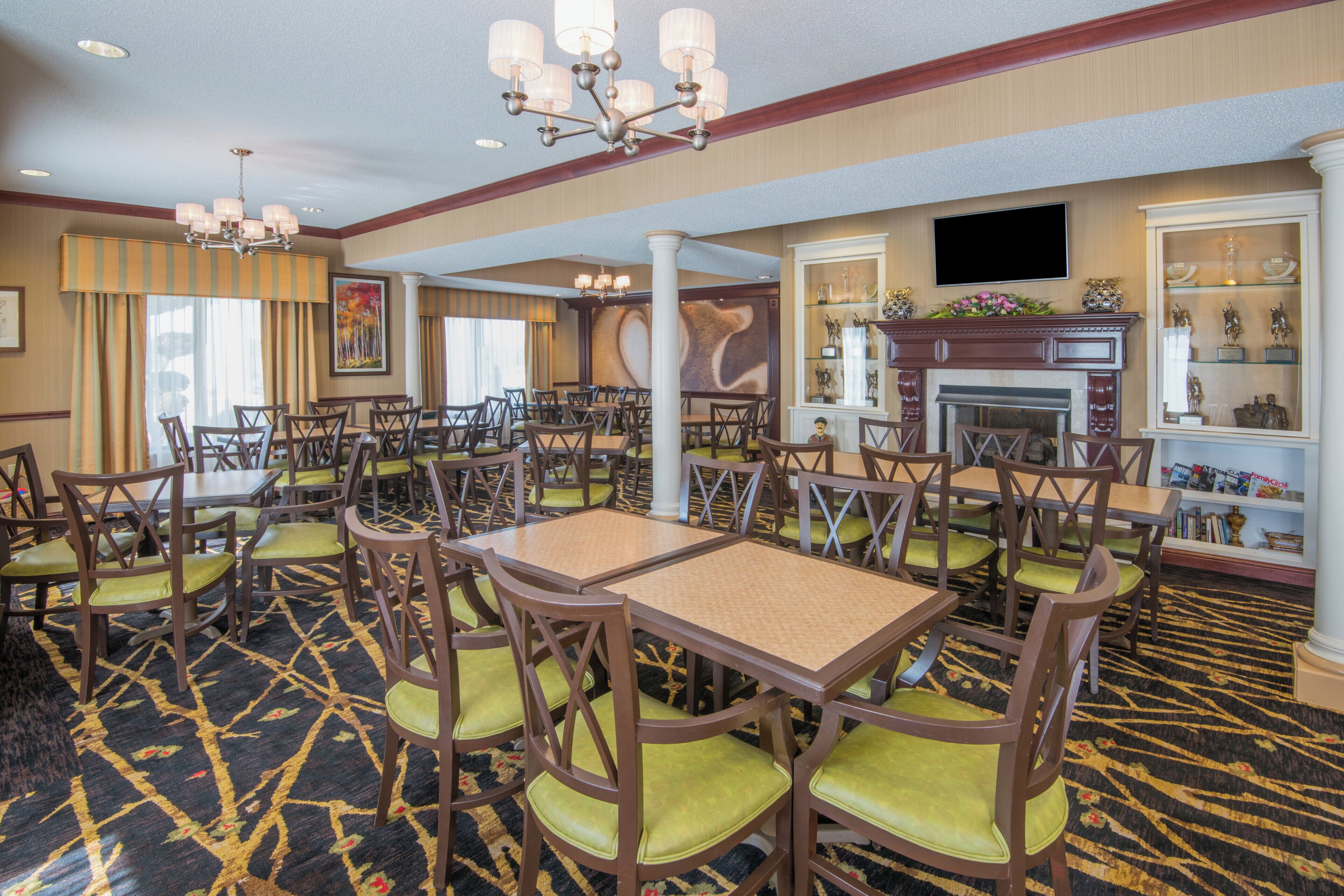 A hotel dining area with multiple tables and chairs, a fireplace, and a television mounted on the wall.