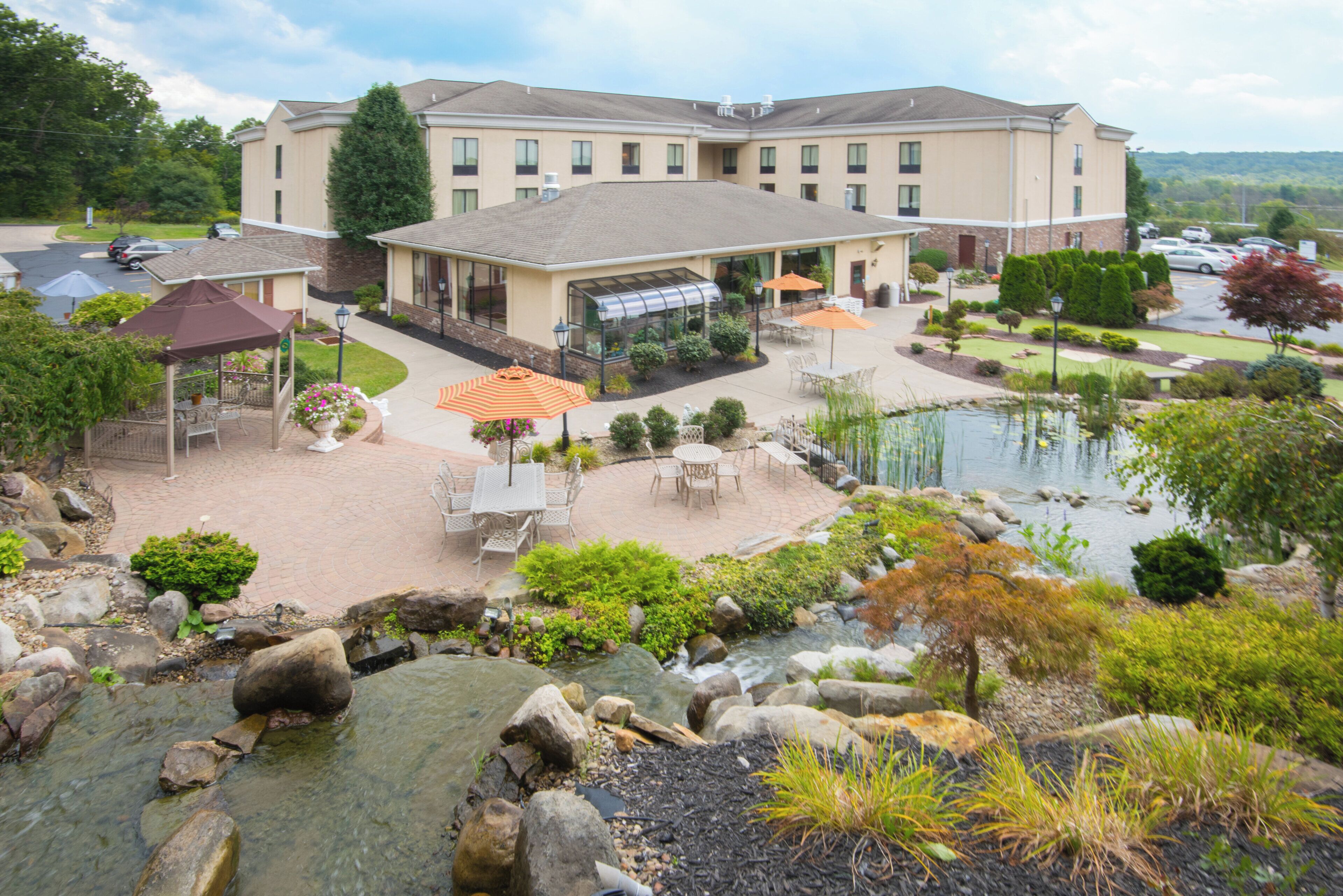 Un hotel con un patio que cuenta con mesas al aire libre, un estanque y un invernadero.