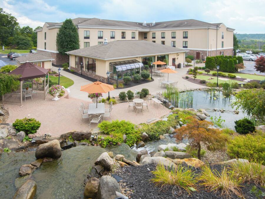 Un hotel con un patio que cuenta con mesas al aire libre, un estanque y un invernadero.