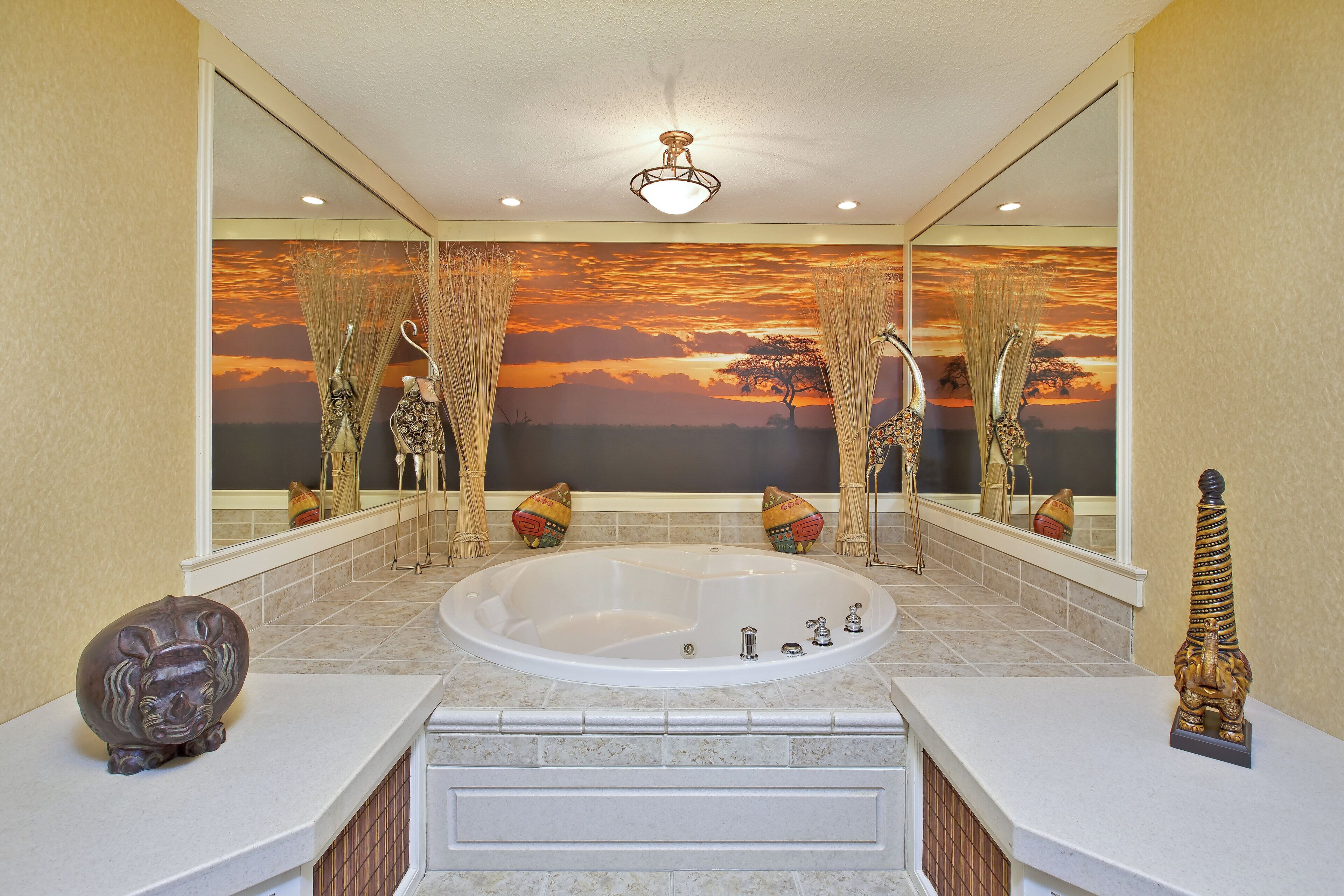 A bathroom with a large bathtub, a mirror, and a sunset mural on the wall.