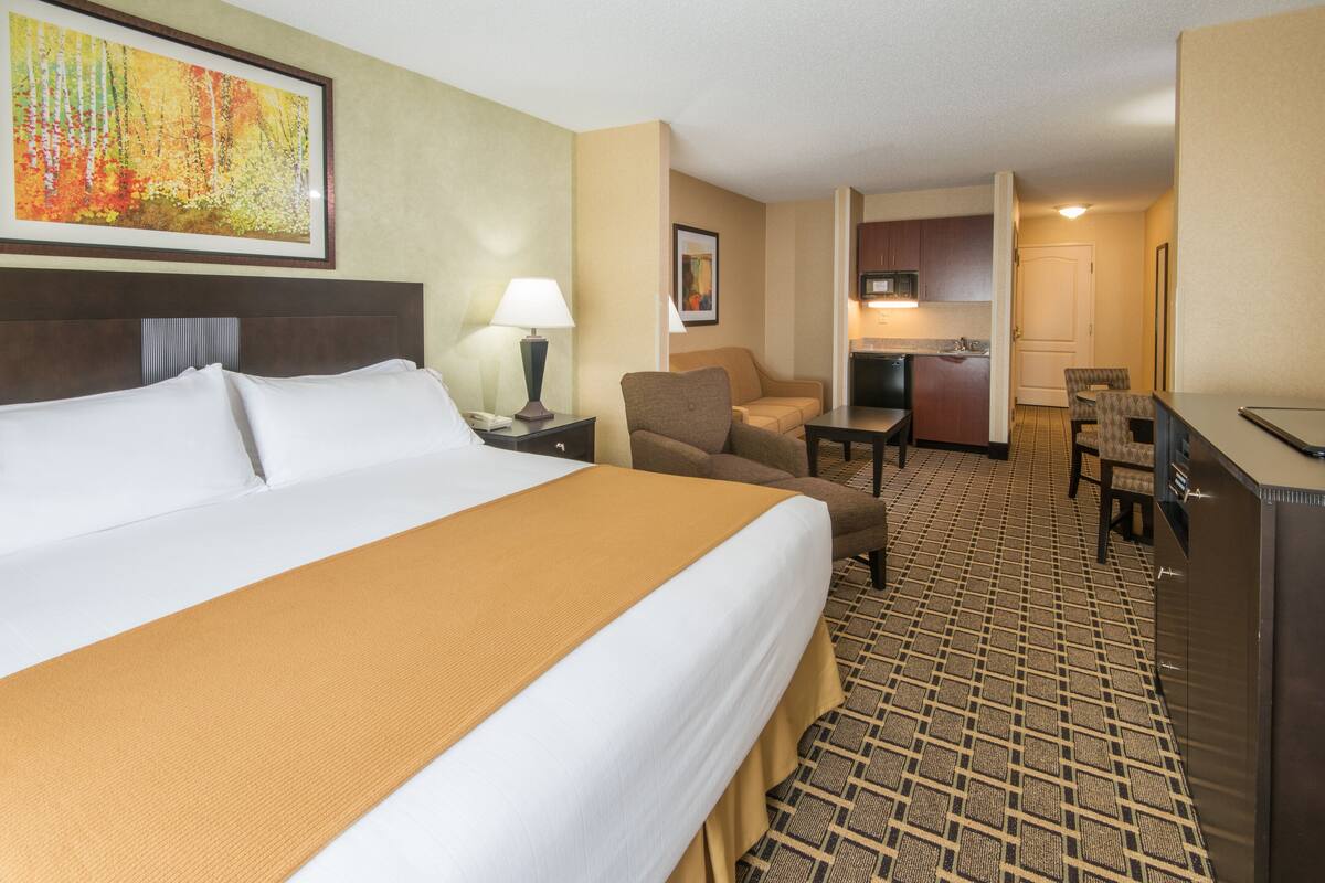 A hotel room with a large bed, a desk, a chair, a small table, and a kitchenette.