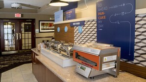 A breakfast station with a flat-top griddle, a sign indicating hot food, and a wall with directional arrows and text. - Holiday Inn Express & Suites Sharon-Hermitage by IHG (West Middlesex)