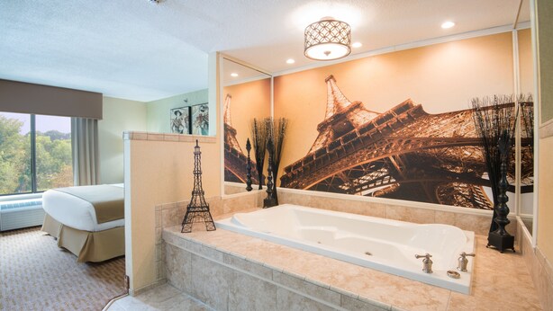 A modern bathroom with a large bathtub, a mirror with an Eiffel Tower mural, and a view of trees through a window.