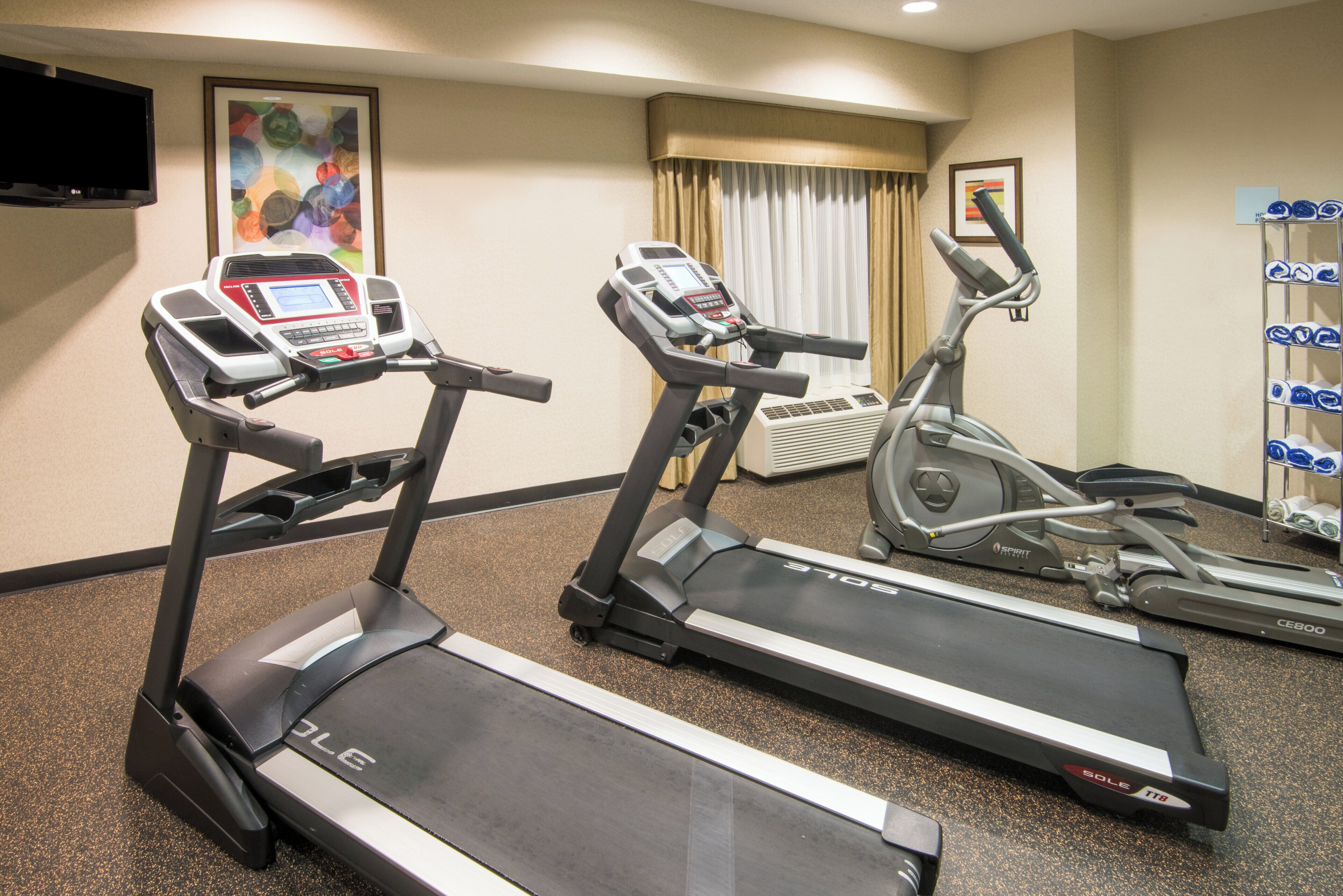 A hotel fitness room with treadmills, a stationary bike, and a wall-mounted TV.