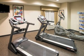 Et hotel fitnessrum med løbebånd, spinningcykel og et tv på væggen.