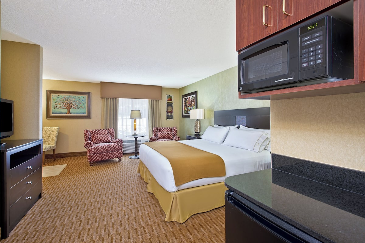A hotel room with a bed, a desk, a chair, a television, a microwave, and a window with curtains.