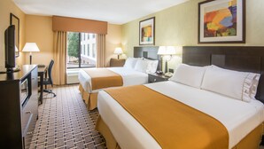 A hotel room with two beds, a desk, a chair, and a TV.