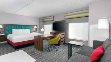 A hotel room with a bed, desk, chair, sofa, TV, and windows.