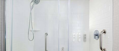 A glass-enclosed shower with a handheld showerhead, a handheld showerhead, and a handheld showerhead.