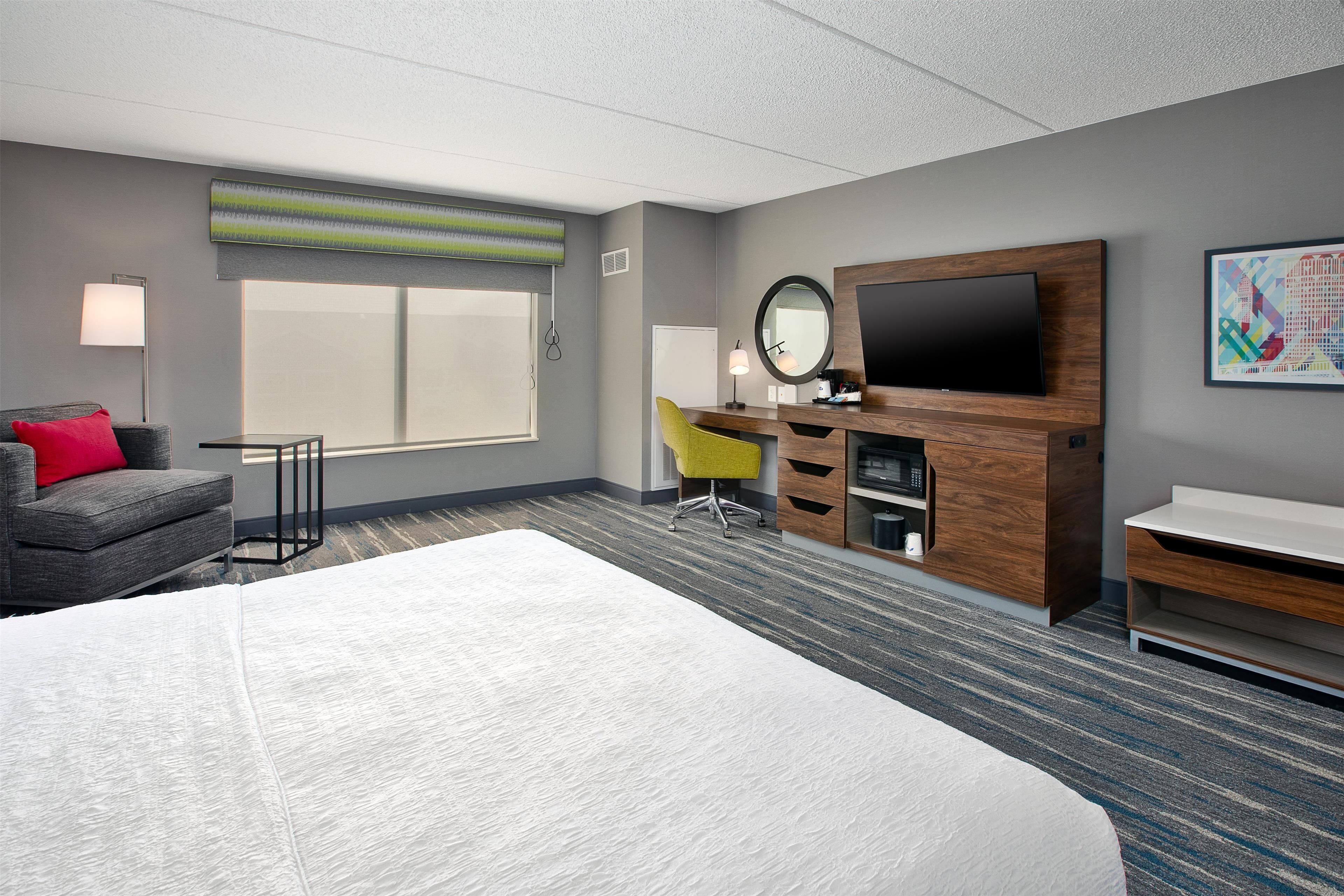 Une chambre d’hôtel avec un grand lit, un bureau avec un ordinateur, une télévision et une chaise.