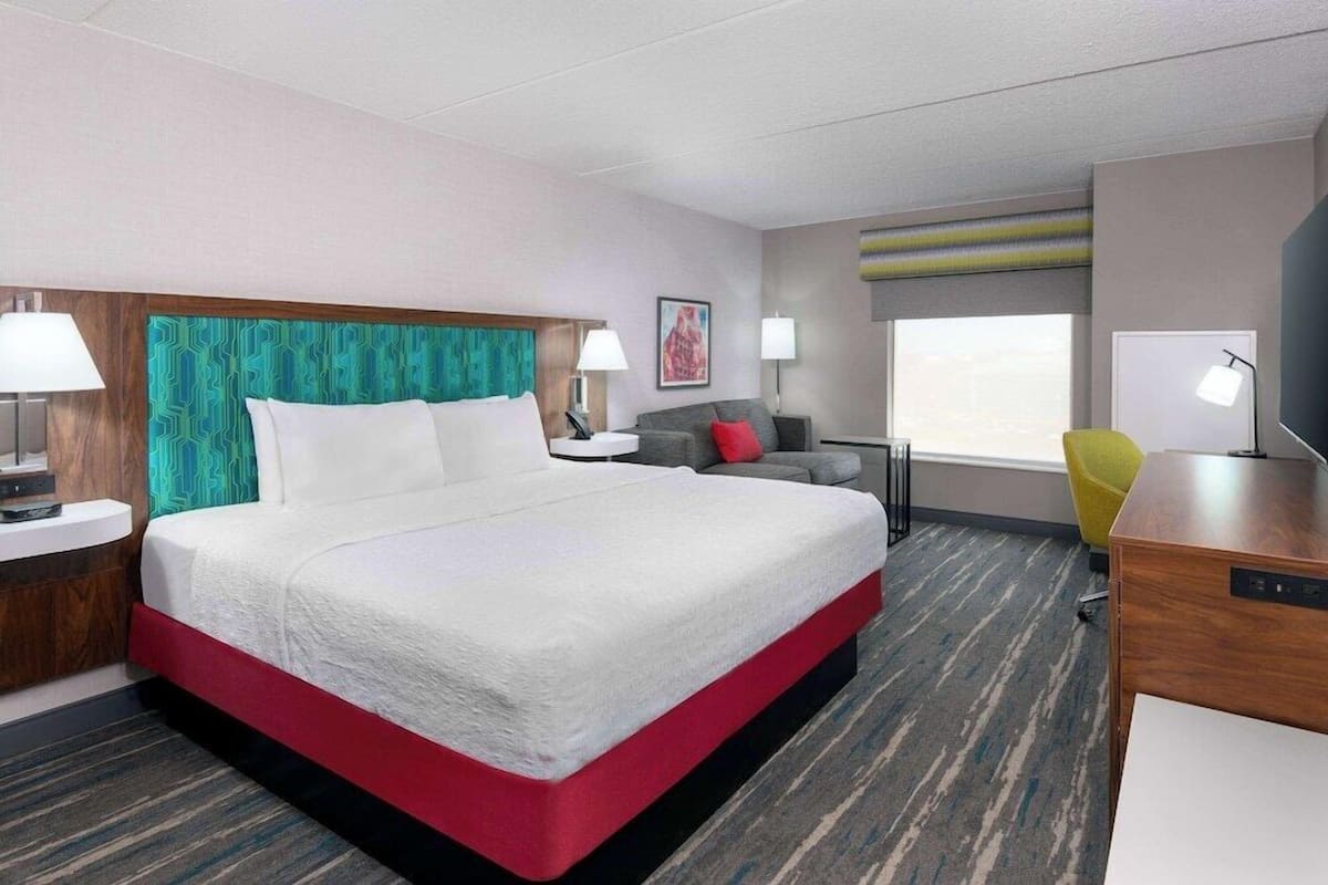 A hotel room with a large bed, a desk, a chair, and a window.