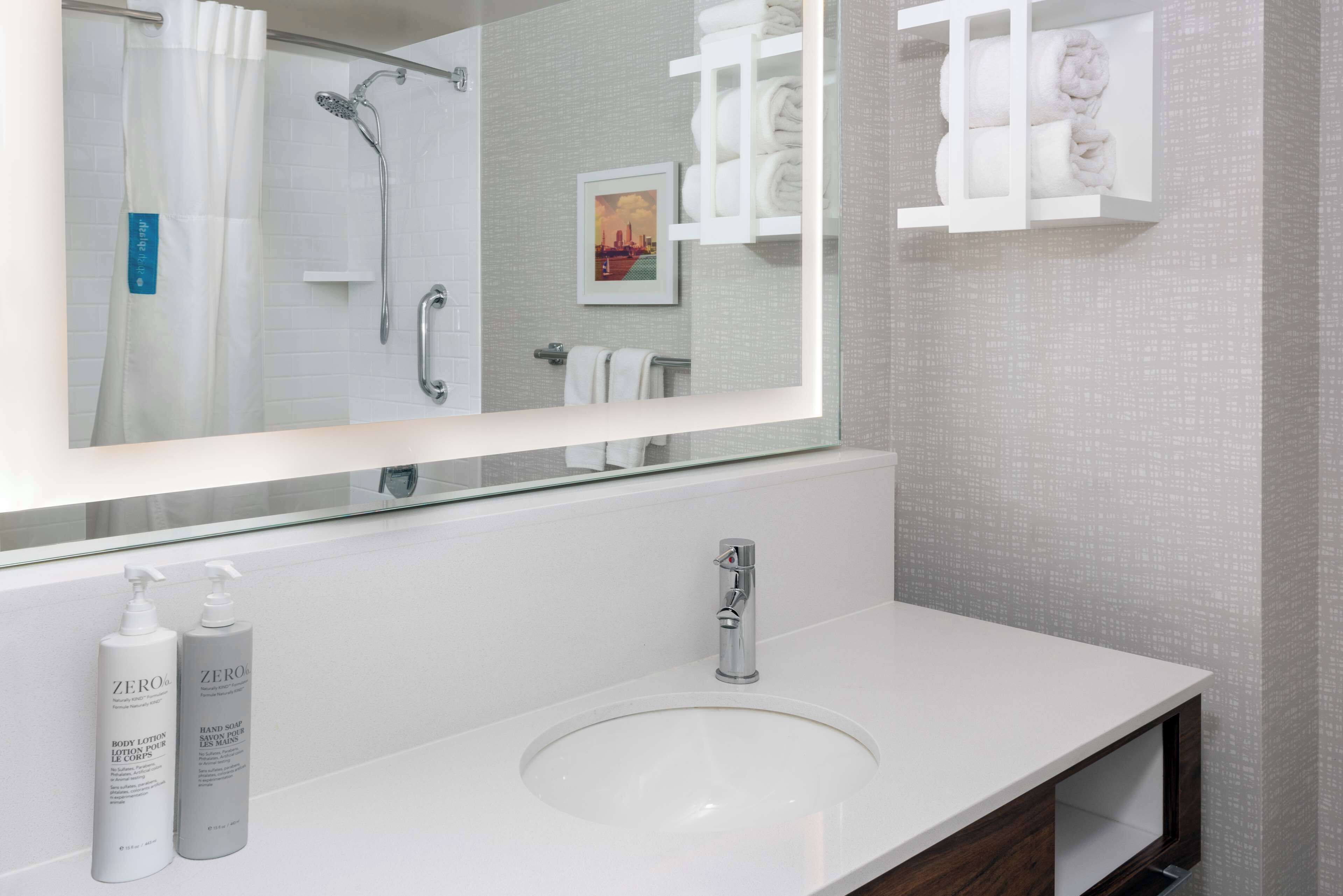 Un bagno moderno con uno specchio grande, un lavandino bianco e due flaconi di lozione corpo Zero.