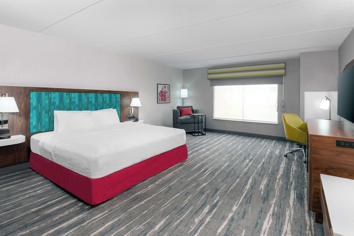A hotel room with a bed, desk, chair, and a window with a view.