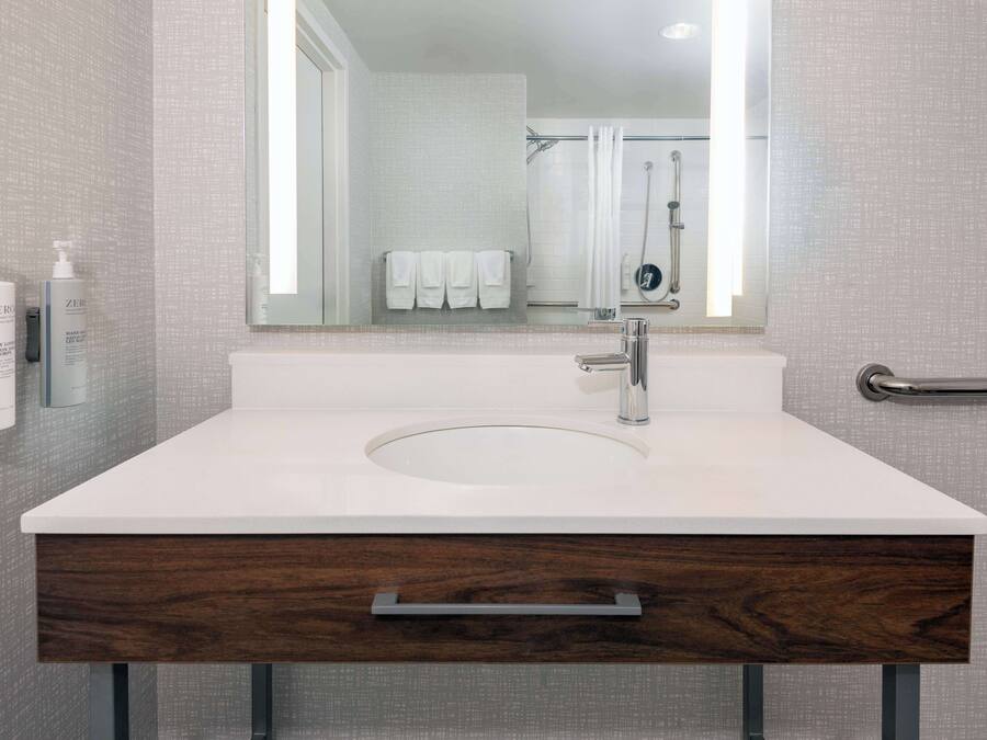 Un baño moderno con un lavamanos blanco, un espejo y una zona de ducha.