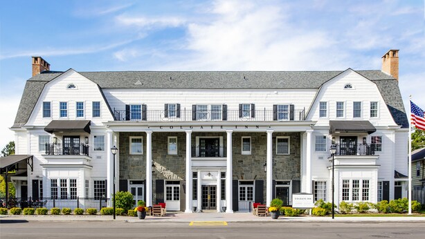 A two-story building with a stone facade, named "Colgate Inn," featuring a central entrance with columns, a flag, and outdoor seating.
