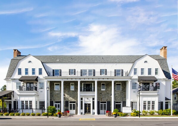 A two-story building with a stone facade, named "Colgate Inn," featuring a central entrance with columns, a flag, and outdoor seating.