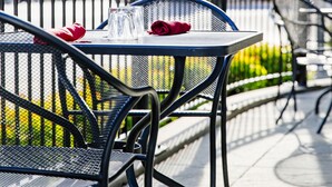 An outdoor seating area with a table and chairs, a railing, and a view of a building with a clock tower. - Colgate Inn (Hamilton)