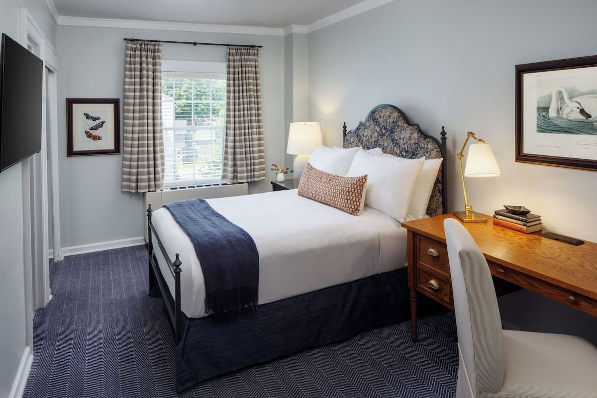 A neatly arranged hotel room with a bed, bedside lamps, a desk, and a chair.