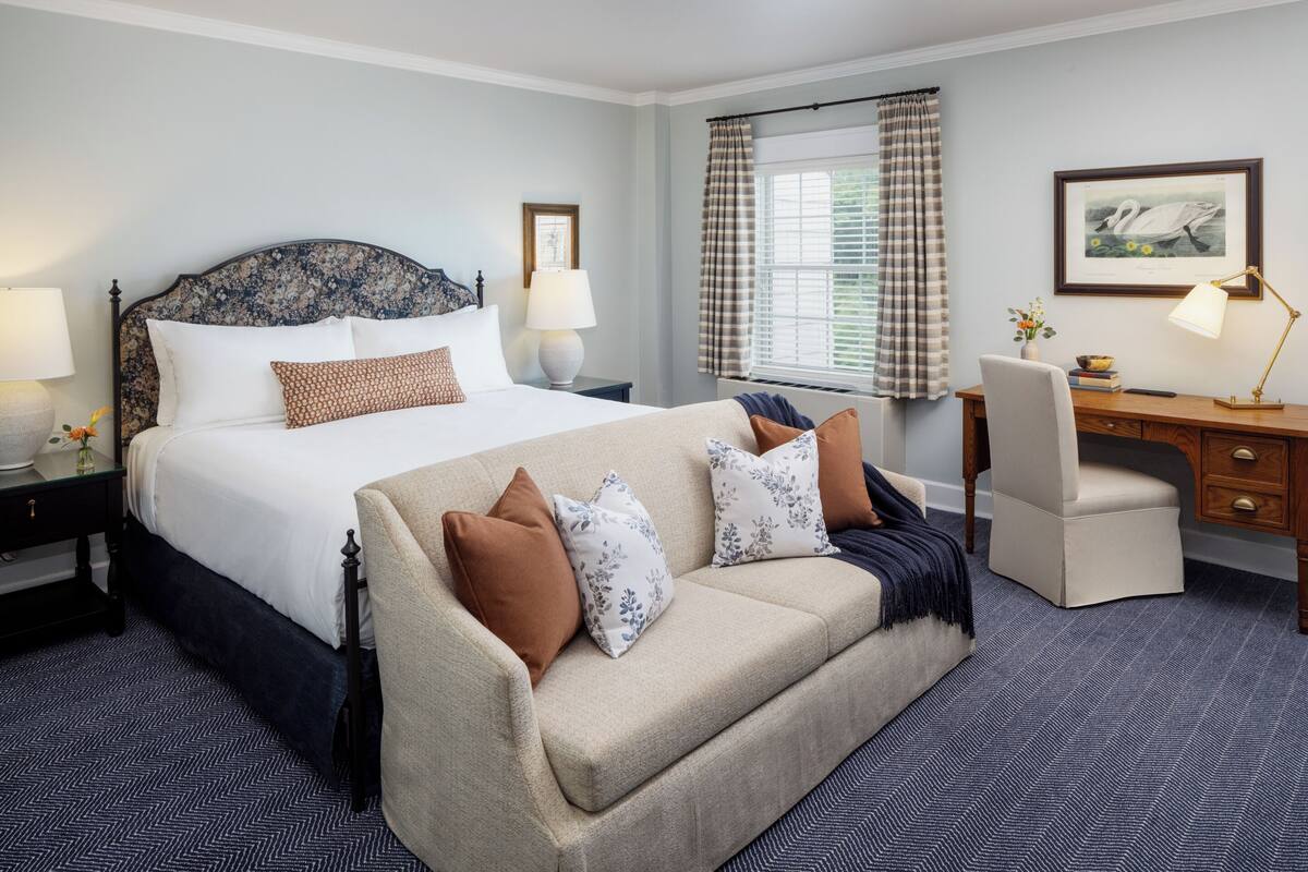 A hotel room with a large bed, a sofa, a desk, and a chair.