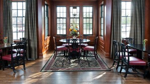 A dining room with a round table, red cushioned chairs, and a floral centerpiece.