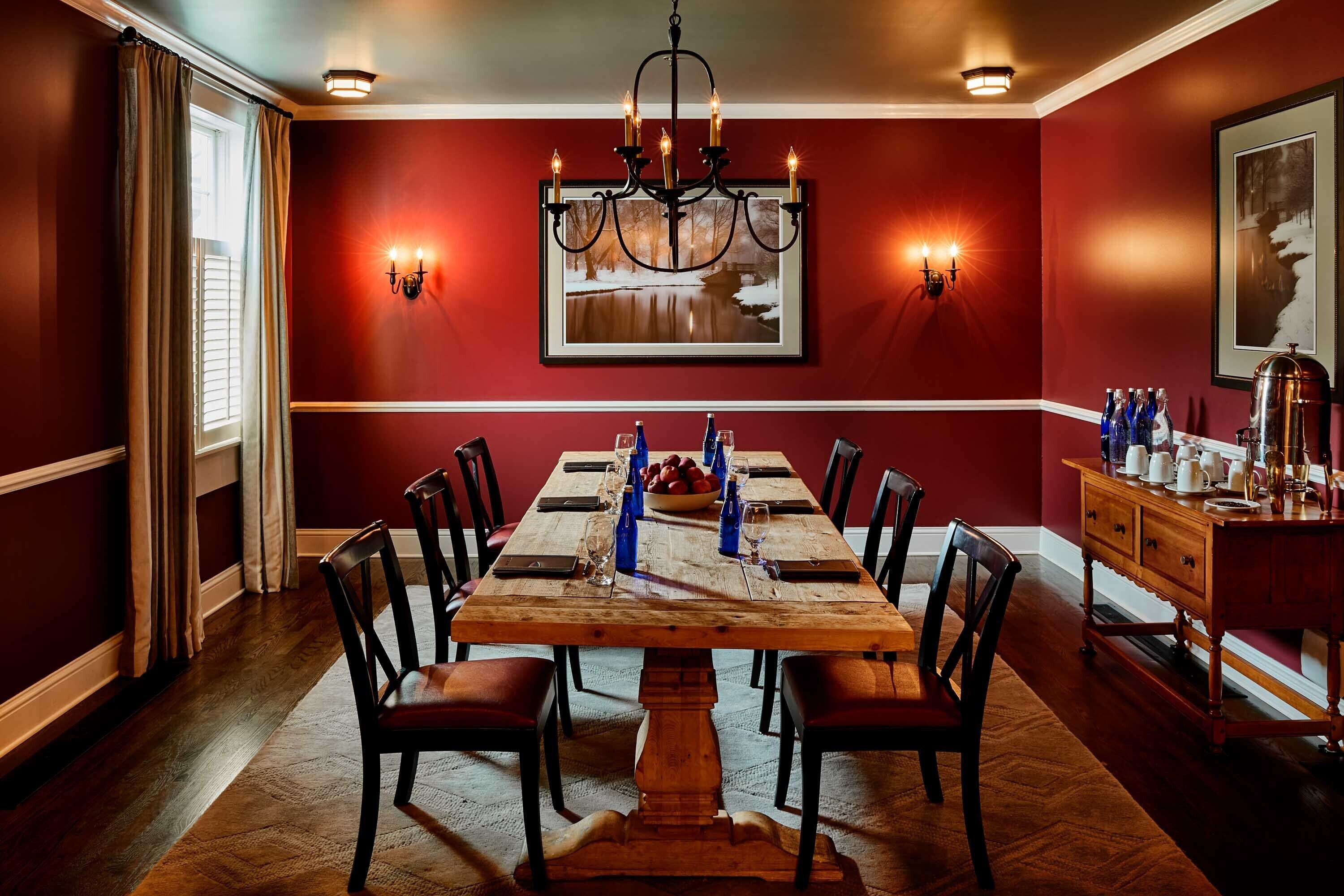 A dining room with a wooden table set for six, surrounded by chairs, a chandelier, and wall sconces.