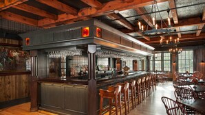 A bar area with a long counter, multiple stools, and a high ceiling with exposed beams. - Colgate Inn (Hamilton)