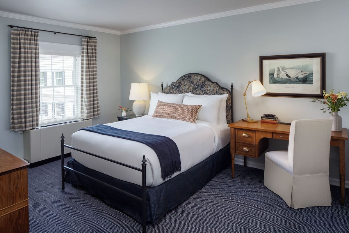 A neatly arranged bedroom with a bed, bedside tables, a desk, and a chair.