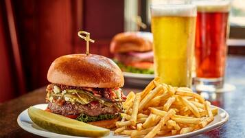 A burger with fries and a pickle on a plate, with a glass of beer in the background.