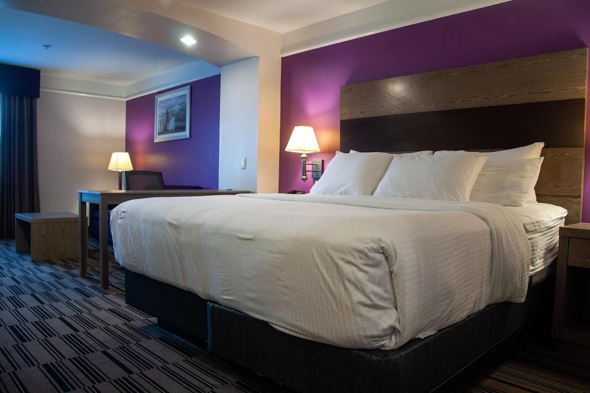 A hotel room with a large bed, bedside tables, a desk, and a wall-mounted lamp.
