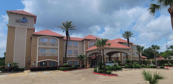 A hotel with a prominent tower, multiple balconies, and a parking lot with palm trees. - Kemah Edgewater Hotel, SureStay Collection by Best Western (Seabrook)