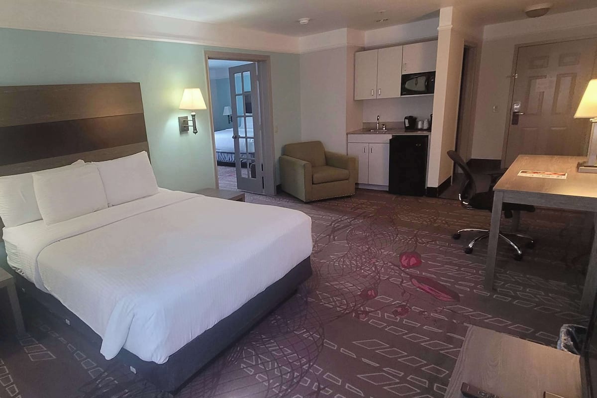 A hotel room with a large bed, a desk, a chair, a microwave, and a kitchenette.