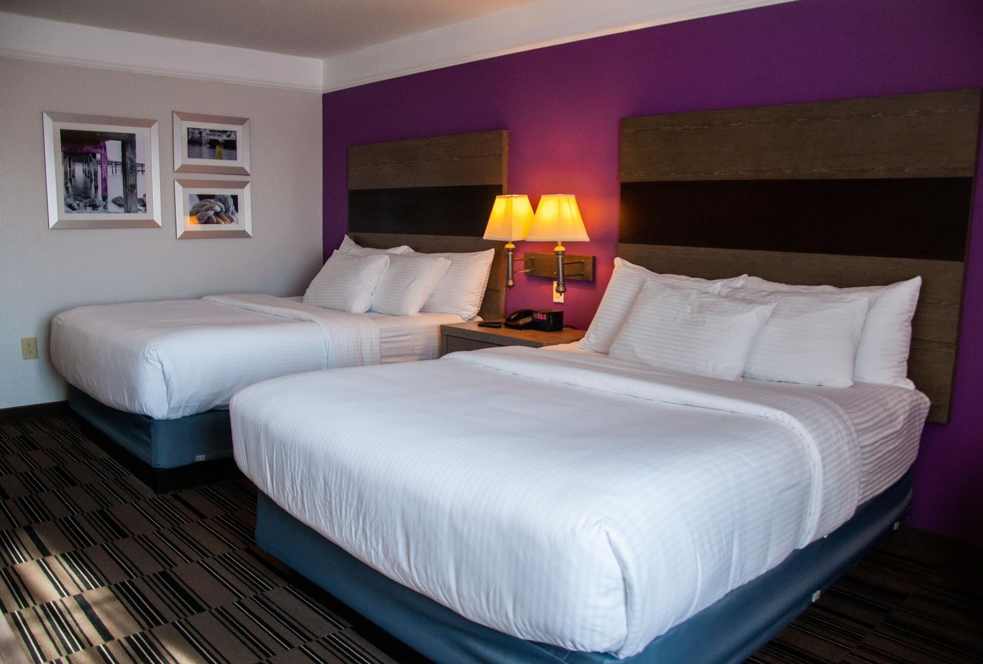 A hotel room with two beds, a nightstand with a lamp, and framed pictures on the wall.